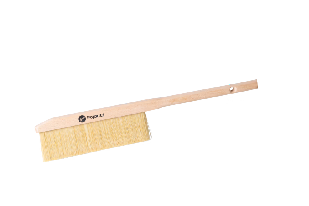 Pajarito_Dummy_Duster long handle P-Line_179114_2024-02 Une brosse en bois avec des poils clairs, dotée d'un manche et d'un logo portant la mention 'Pajarito'. La brosse est positionnée avec le côté des poils tourné vers la gauche, sur un fond blanc.