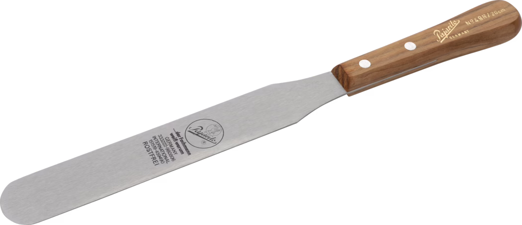 Pajarito_Dummy_Colour knife _036121_2021-02 Une spatule en acier inoxydable avec un manche en bois, gravée avec le nom de la marque et les détails du produit. La spatule a une lame plate idéale pour retourner et servir des aliments.