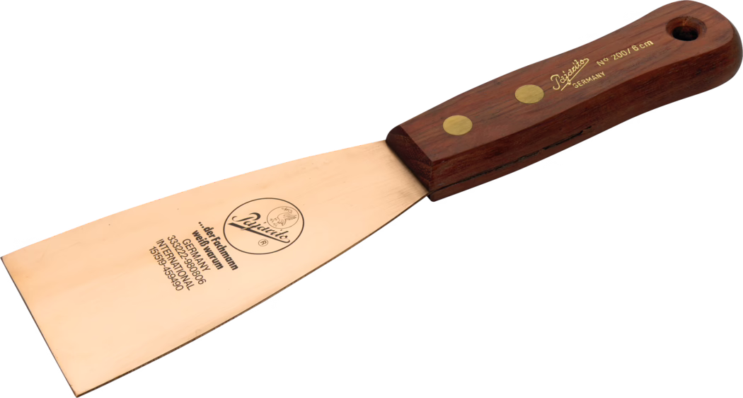 Pajarito_Dummy_Beryllium spatula wood handle_012868_012869_012870_2021-02 Gros plan d'un outil à main : une spatule de peintre à large lame métallique couleur cuivre et manche en bois foncé fixé par deux rivets en laiton. La lame porte un logo et des inscriptions, notamment 'Germany' et la mention de taille 'No 200 / 8 cm', et présente de légères rayures et un biseau tranchant. Le manche est arrondi et ergonomique, avec un trou d'accrochage à l'extrémité ; l'outil est photographié sur fond blanc.